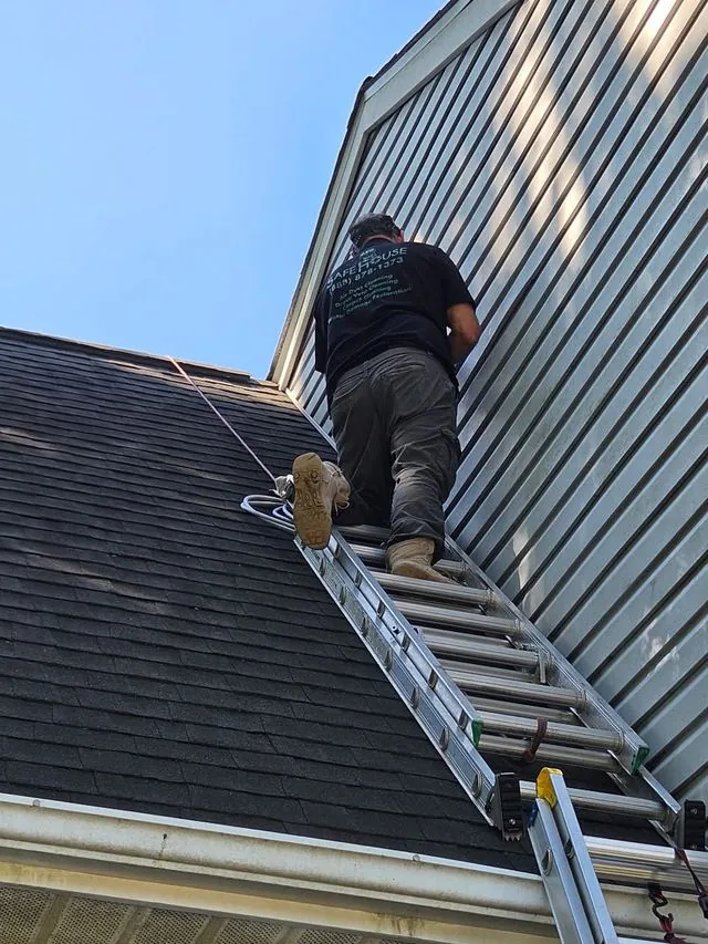 A technician on a ladder reaching a second-storey roof-terminating dryer vent